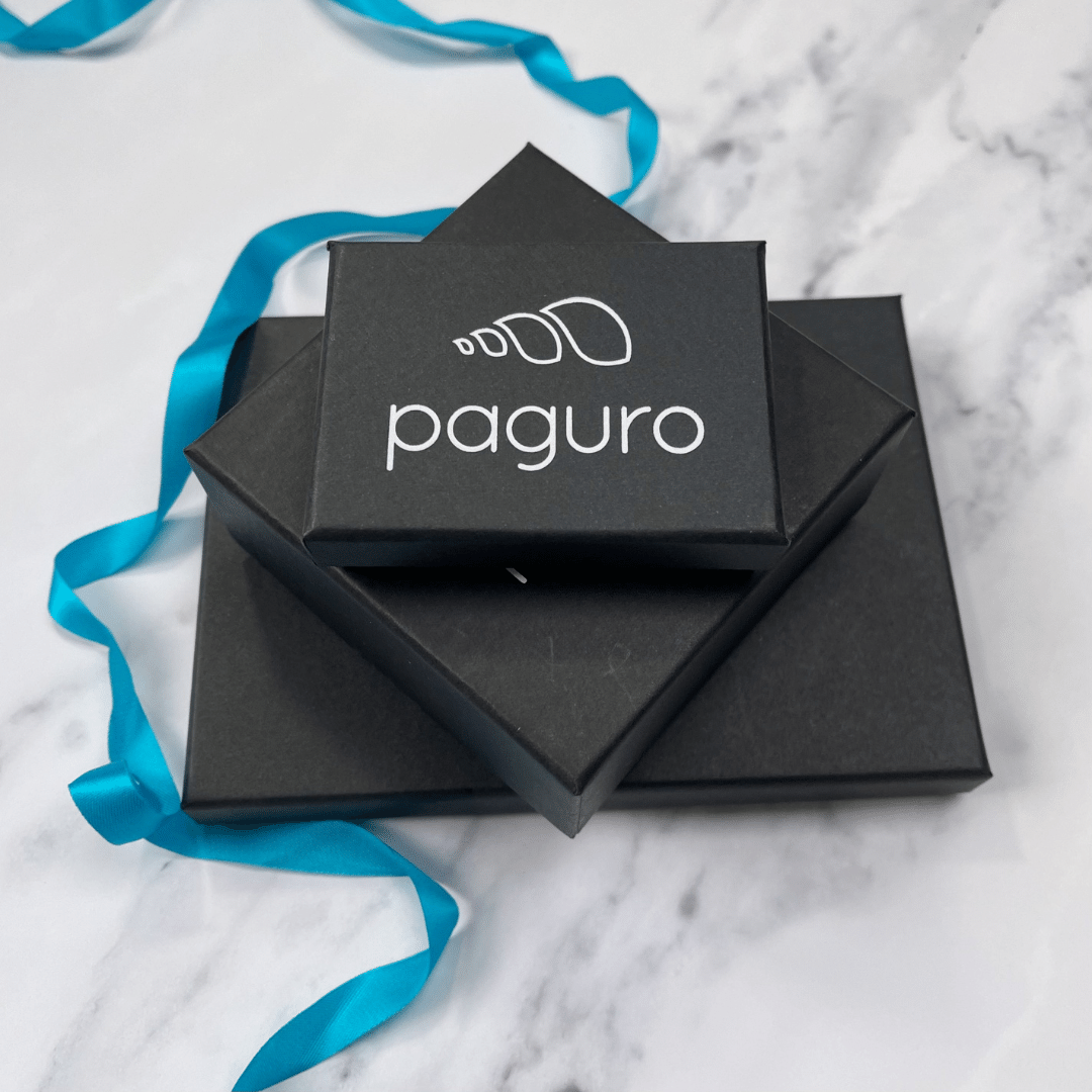 Black Paguro Upcycle boxes stacked on marble surface with blue ribbon for recycled rubber earrings