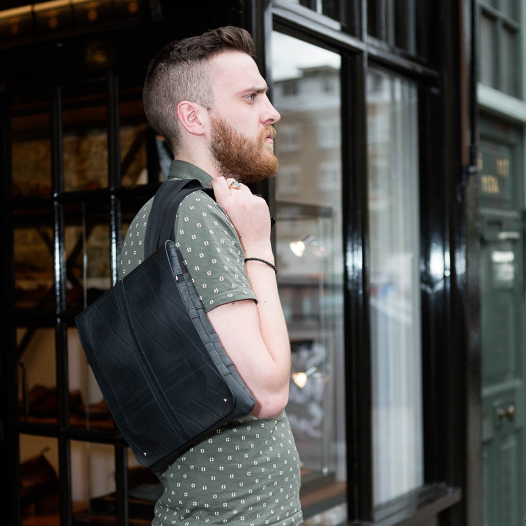 Paguro Upcycle recycled rubber crossbody bag worn by man standing outdoors near glass window