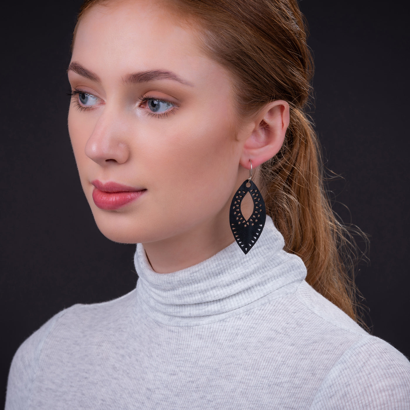 Woman wearing black recycled rubber earrings by Paguro Upcycle with intricate cutout design